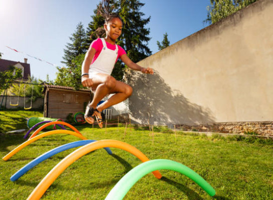 Happy beautiful black girl jump over line of obstacles on the lawn Young girl jumping over hurdles